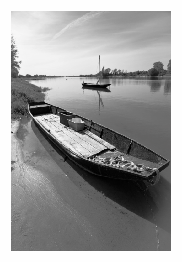 A beached flat-bottomed boat leading the eye out to a small masted boat anchored in the Loire at Montjean, black and white