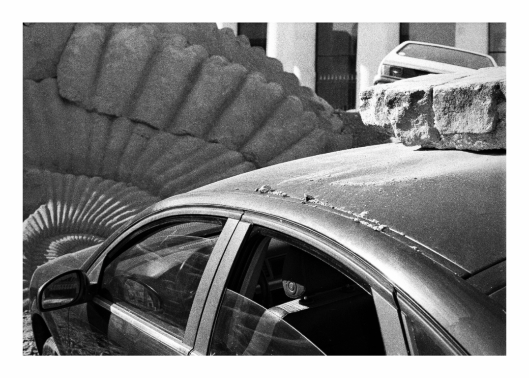 A carved stone ammonite the size of a tractor wheel set into a Nantes pavement beside a parked estate car, black and white