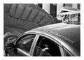 A carved stone ammonite the size of a tractor wheel set into a Nantes pavement beside a parked estate car, black and white