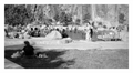 People sitting on grass and white rock ledges beside the quarry pool at the Jardin Extraordinaire in Nantes, cliff face behind, black and white