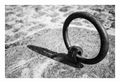 A hand-forged iron mooring ring bolted into the stone quay at Montjean-sur-Loire, casting a hard shadow across the granite, black and white