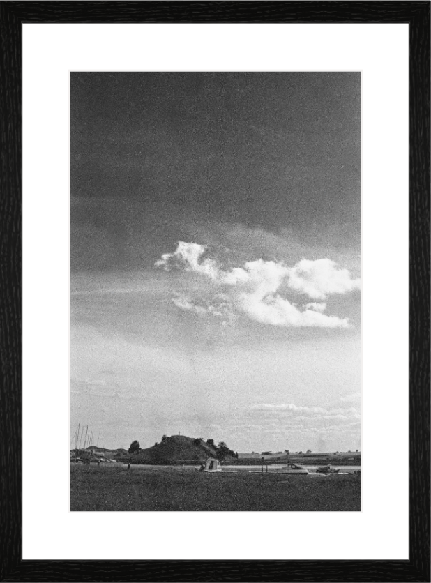 A bright stack of cumulus cloud filling the sky above the low green mound of Church Hill at Alnmouth, grainy black and white