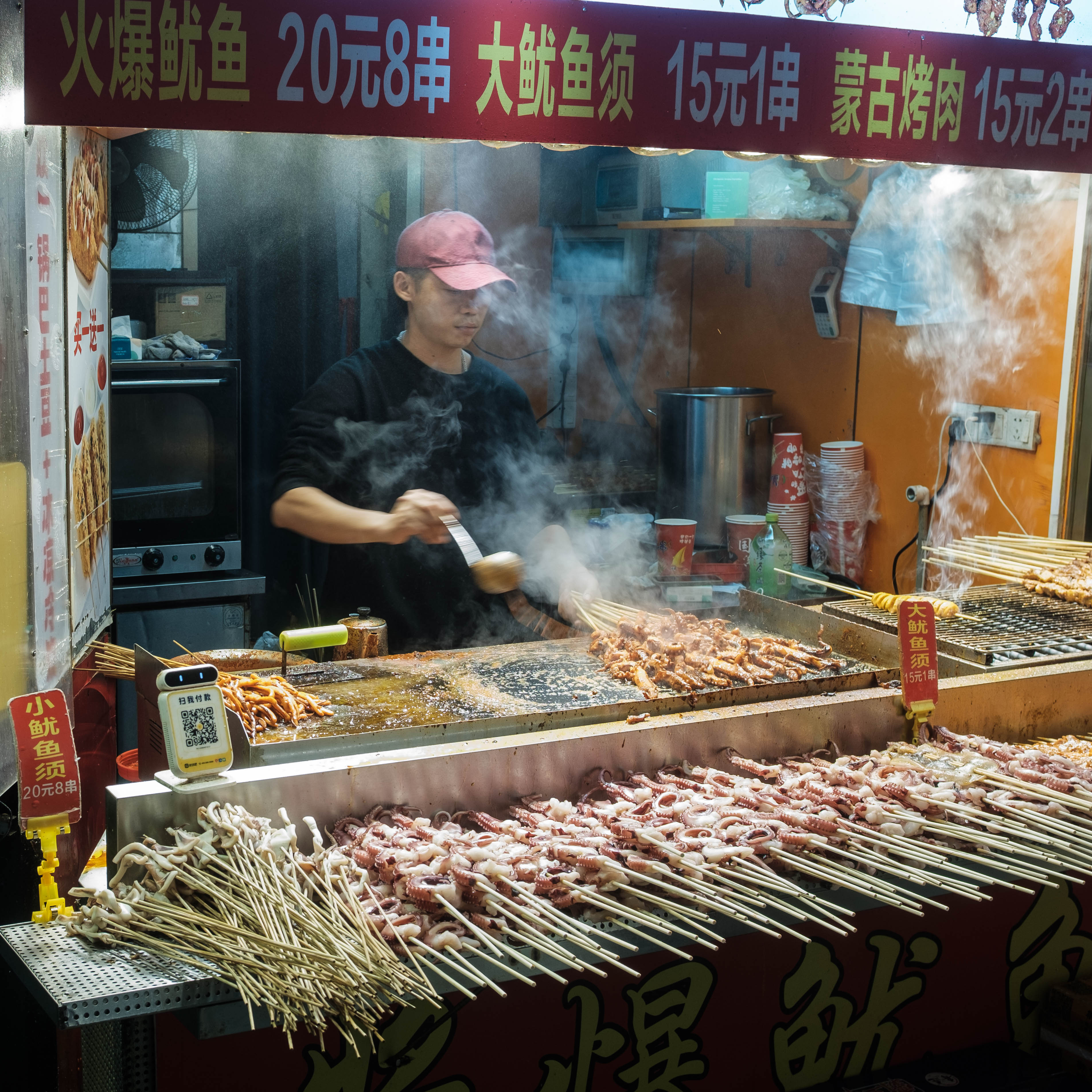 A Shenzhen night market stall wreathed in steam, skewers over the flame and a cook working behind them