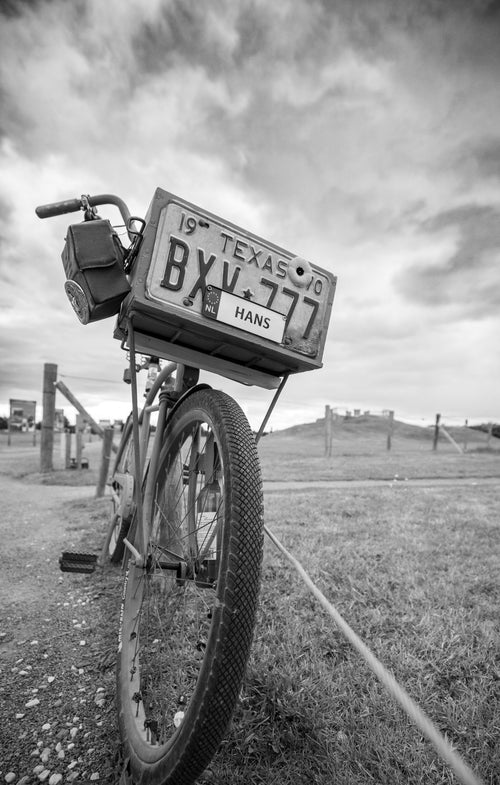 A bicycle leaning at the Merville Battery carrying a 1940 Texas licence plate and a poppy, Normandy