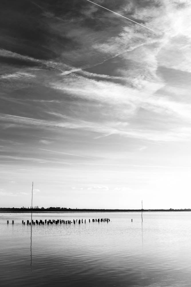 Marker beacons standing in shallow water on the Passage du Gois in the Vendée under an open sky, black and white