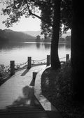 A paved path curving around Huizhou Lake in China towards a lakeside pavilion among trees